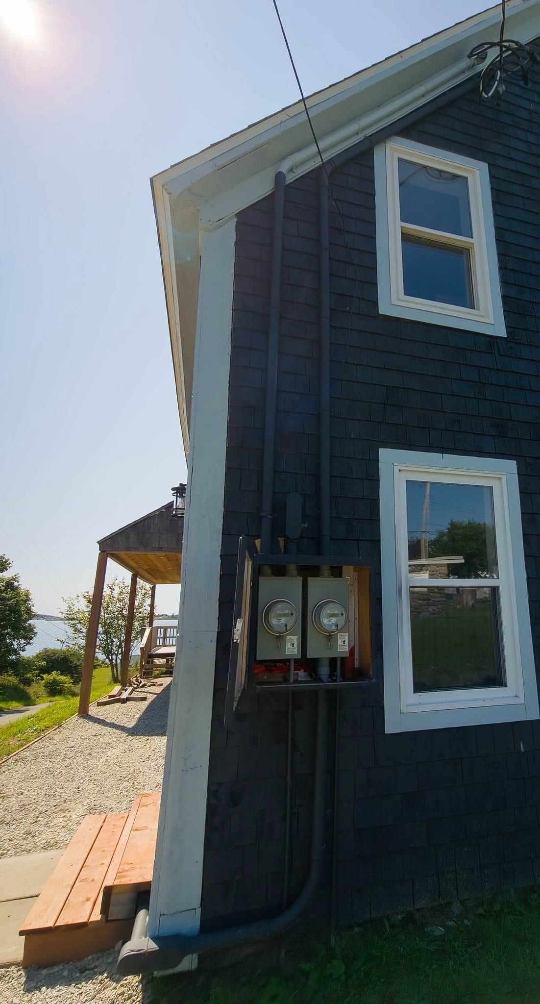A dark-clad coastal home with its exterior electrical service run up the gable end.