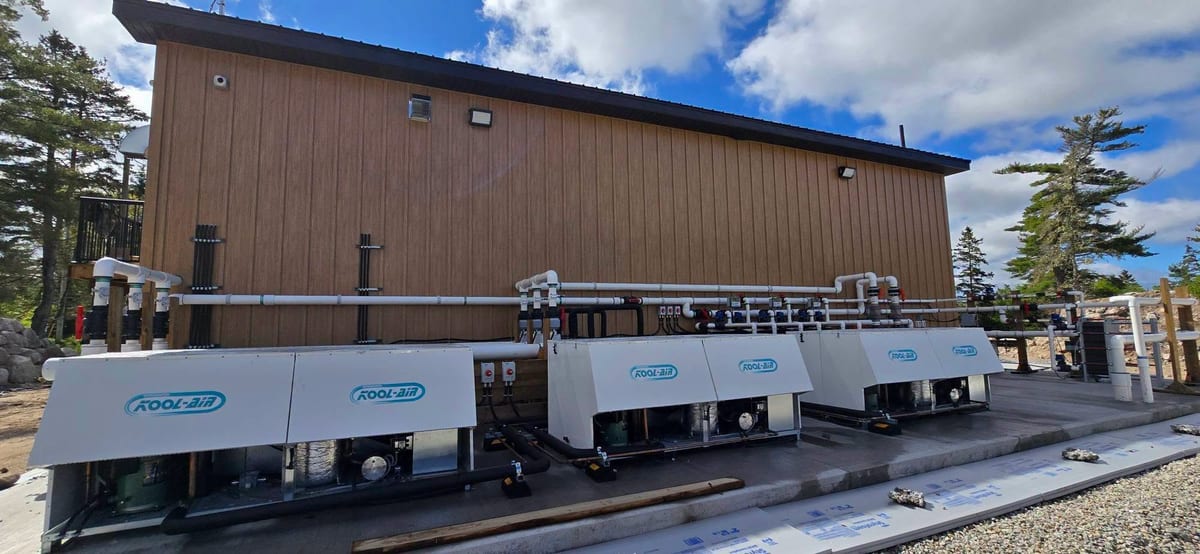 A row of heat pump condensers on a commercial building with their electrical feeds run alongside.