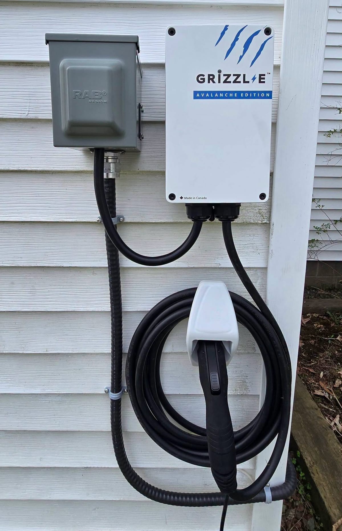 A Grizzl-E electric vehicle charger mounted on house siding with its disconnect beside it.