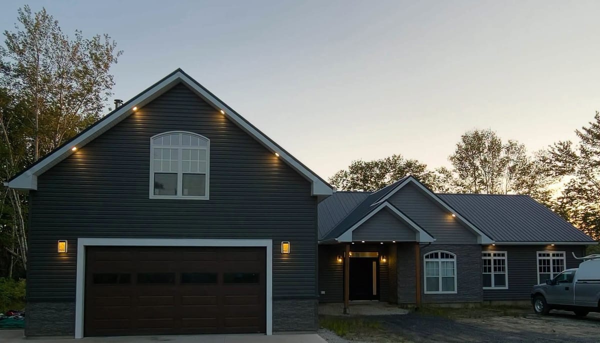 A home and attached garage at dusk with exterior and soffit lighting on.