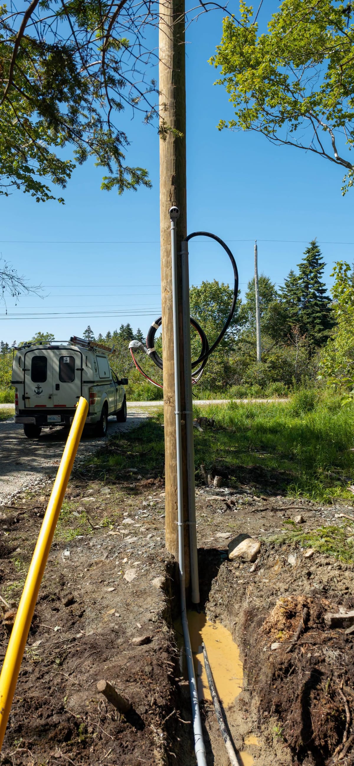 A bucket truck at a utility pole with the trench and conduit open for a new underground service.