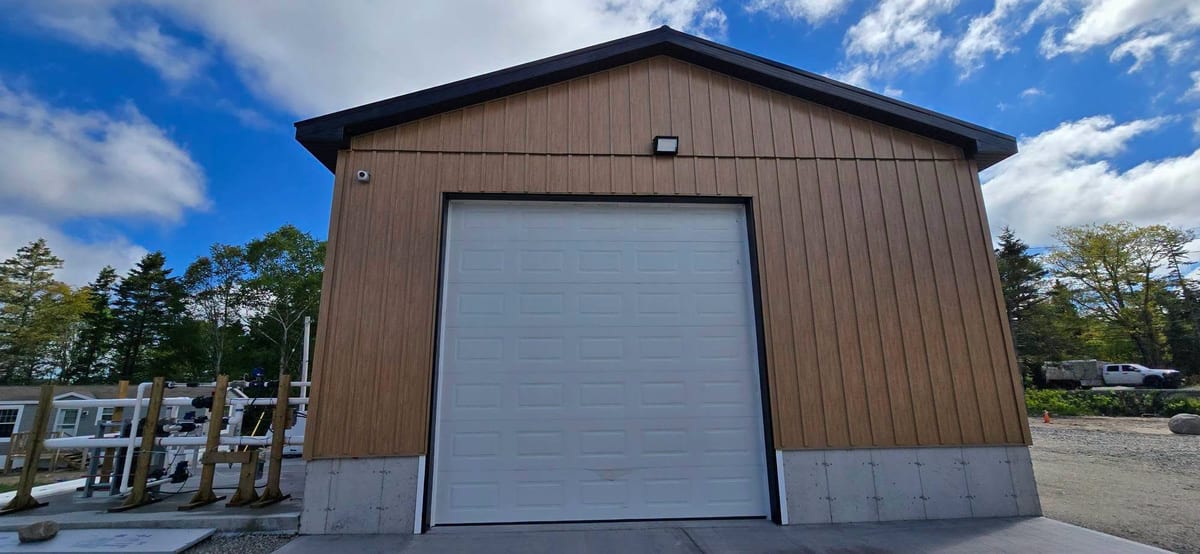 A steel commercial building with an overhead door and exterior lighting.